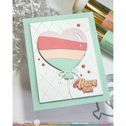 A handmade greeting card featuring a layered heart-shaped balloon design in pastel pink, peach, and mint green, with the words 'Have fun' in gold foil. The card is styled on a white surface with craft tools and paper tinsel in the background.