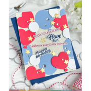 A handmade layered paper birthday card with red, white, and blue balloon shapes, silver glitter accents, and decorative text reading 'TODAY IS YOUR DAY Have fun Celebrate every little moment! Happy Birthday,' shown on a white wood background with small floral props and ribbon.