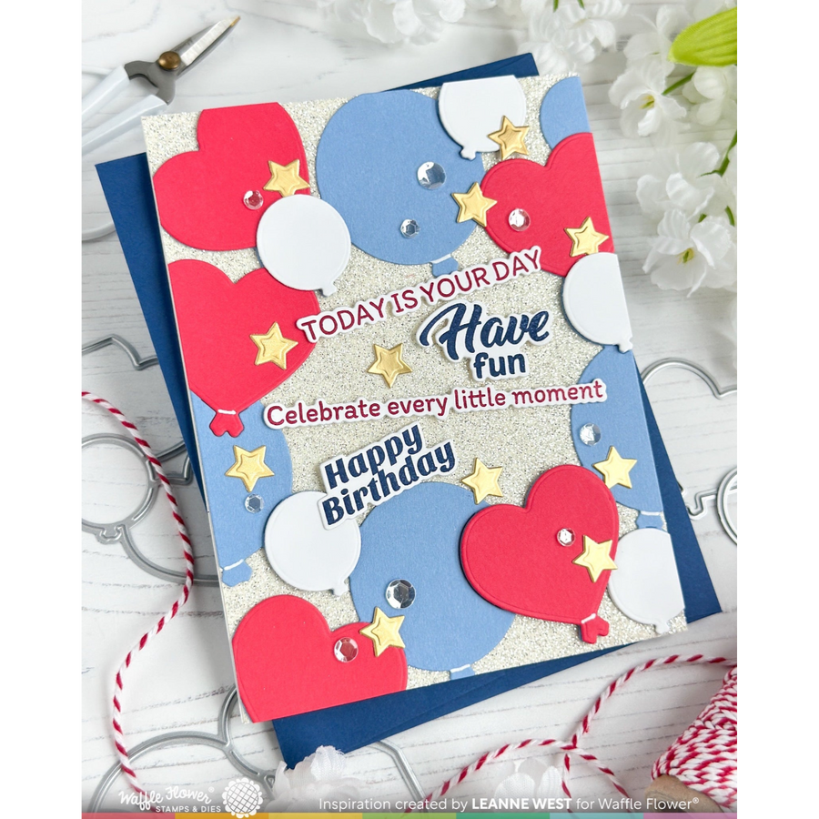 A handmade layered paper birthday card with red, white, and blue balloon shapes, silver glitter accents, and decorative text reading 'TODAY IS YOUR DAY Have fun Celebrate every little moment! Happy Birthday,' shown on a white wood background with small floral props and ribbon.