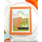 A handmade layered card featuring a die-cut moose wearing an orange scarf against a mountain background, styled on a white beaded plate with an orange leaf in the corner.