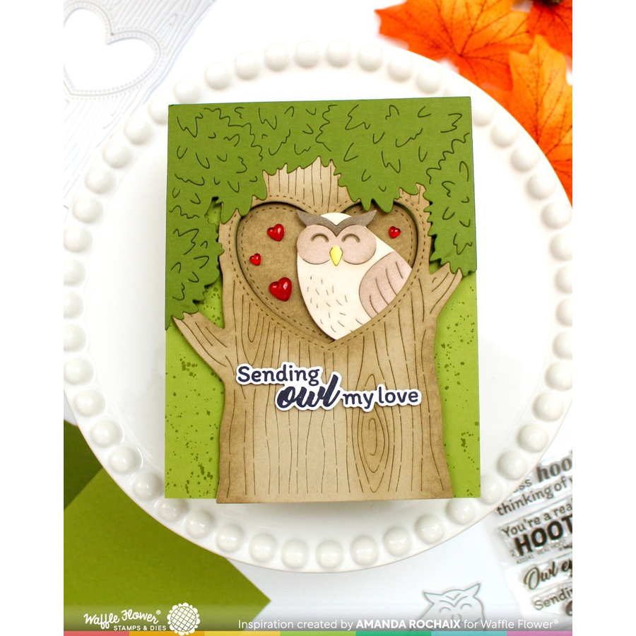 A handmade layered card featuring a brown tree trunk base with a die-cut owl cutout layered over green textured leaves. The card has the text 'Sending owl my love' and is displayed on a white beaded plate with autumn leaves in the corner.
