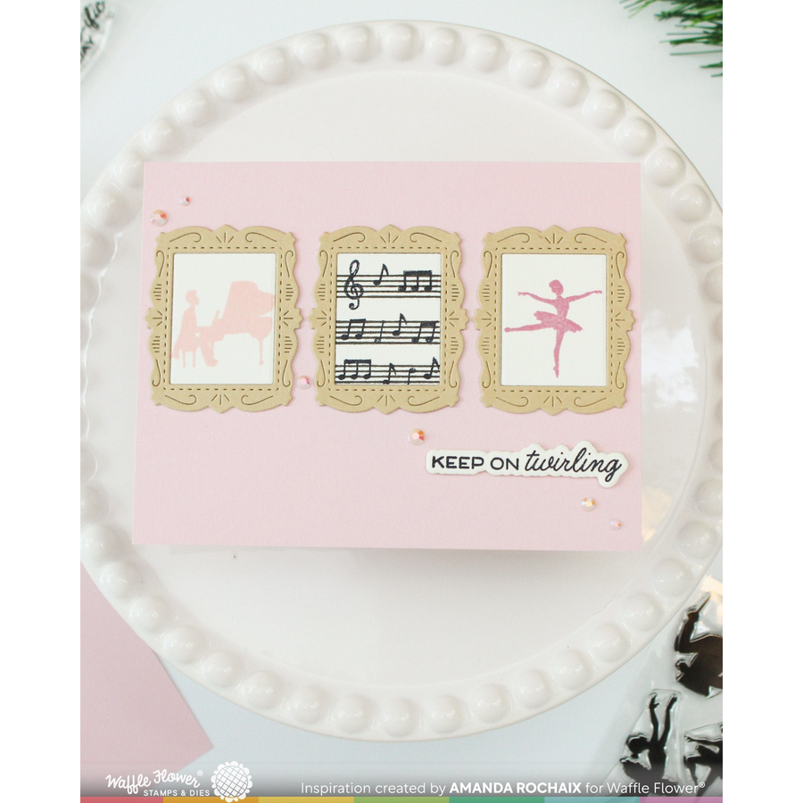 A handmade greeting card with a light pink background, featuring three decorative gold frames containing whimsical illustrations (a camel, musical notes, and a ballerina), with the text 'KEEP ON twirling' in black and white. The card is displayed on a white beaded plate.