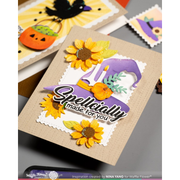 A handmade Halloween-themed greeting card displayed on a gray surface, featuring a kraft beige base, a purple witch hat, yellow sunflowers, green leaves, and the phrase 'Spellcially made for you.' Other cards are partially visible in the background.