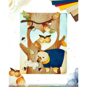 A handmade layered card featuring a heart-shaped cutout in the center of a tree with an owl and a bear, with the word 'Hugs' in script. The card is displayed on a white background with craft paper accents.