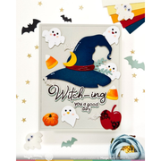 A Halloween-themed layered card or craft design featuring a large navy witch hat with a yellow crescent moon and red band, surrounded by white ghosts, candy corn, a small pumpkin, a red apple, bats, and the text 'Witching you a good day' on a cream background.