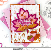A handmade layered card featuring a large pink and orange autumn leaf with the phrase 'Grateful for you!' in white script, surrounded by pink envelopes, acorns, and decorative embellishments on a white background. Text at the bottom reads 'Arsenia Wolf for Pretty Pink Posh'.