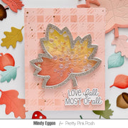 A handmade autumn-themed card featuring a glittery silver maple leaf with a yellow, orange, and pink gradient center filled with clear bubble elements. The card has a pink checkerboard patterned background and the text 'LOVE fall MOST OF all'.