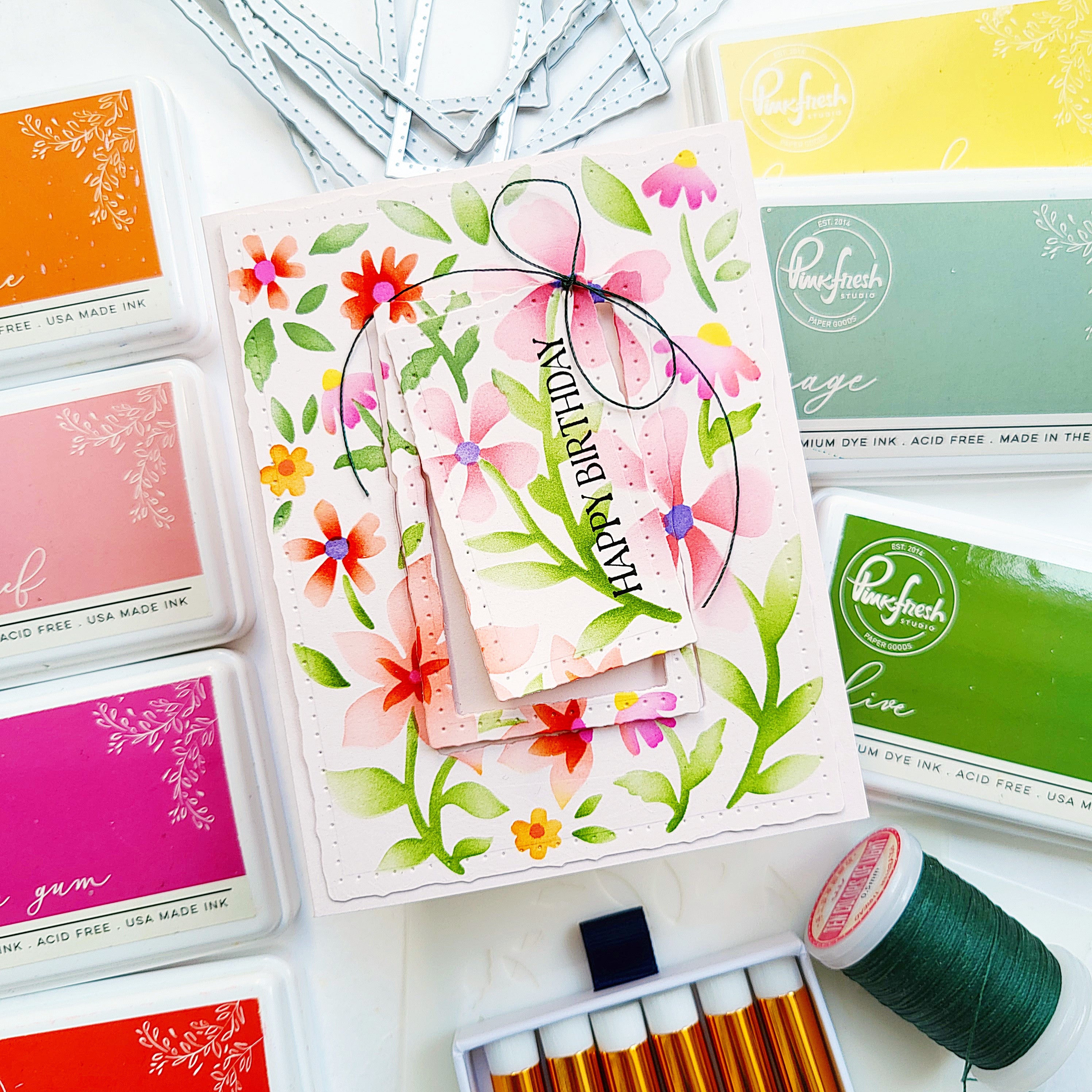 Card with floral design and 'Happy Birthday' text, surrounded by ink pads and thread on a white background