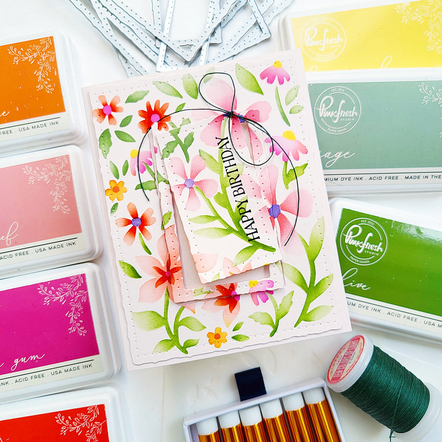 Card with floral design and 'Happy Birthday' text, surrounded by ink pads and thread on a white background