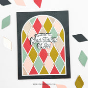 A handmade layered card featuring a black embossed border, a white arched background, and a colorful diamond pattern in red, green, pink, and gold. The center has a die-cut layer reading 'Sending You Glad Tidings of Joy' with a small bow.