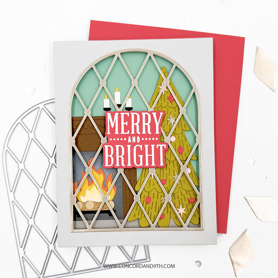 A handmade layered card featuring a festive holiday design with a fireplace, a Christmas tree, and the words 'MERRY AND BRIGHT' in layered paper, shown with a red envelope on a white background.