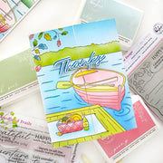 A colorful handmade greeting card featuring a pink rowboat on blue water with the word 'Thanks' in large script, surrounded by other cards and craft papers on a white surface.