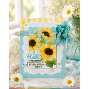 A handmade greeting card featuring yellow sunflowers, green leaves, and turquoise accents, styled with white daisies and a decorative jar in a soft, bright setting.