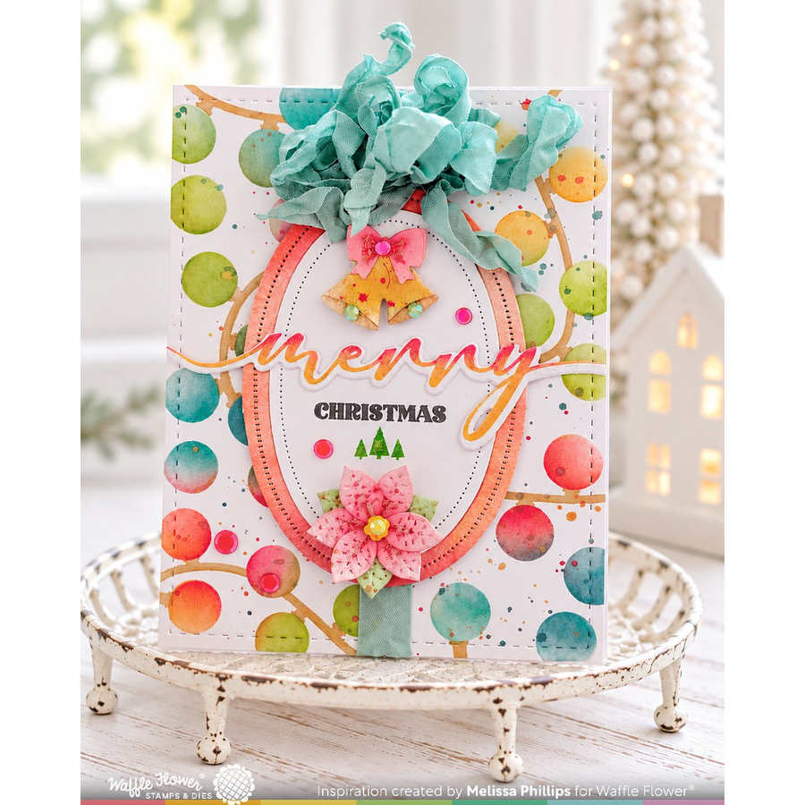 A handmade Christmas greeting card displayed on a distressed white tray. The card features a white background decorated with colorful watercolor-style polka dots in teal, green, orange, and pink, a large orange oval frame, the word 'merry' in elegant gold script, 'CHRISTMAS' in black block letters, and a pink paper flower with a green stem.