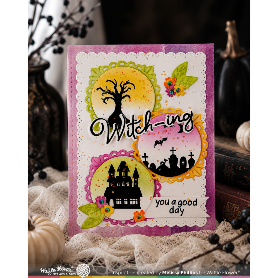 A handmade greeting card with a Halloween theme, featuring the words 'Witch-ing' and 'you a good day', decorated with a black tree, a haunted castle, bats, and autumn leaves on a purple and white scalloped background. The card is styled on a rustic surface with lace, pumpkins, and books.